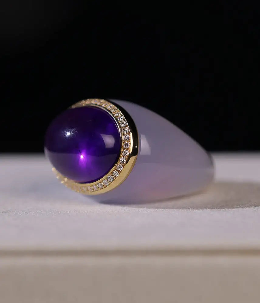 Elegant ring featuring a deep purple cabochon gemstone set in a gold band adorned with sparkling diamonds, complemented by a smooth lavender jade body.
