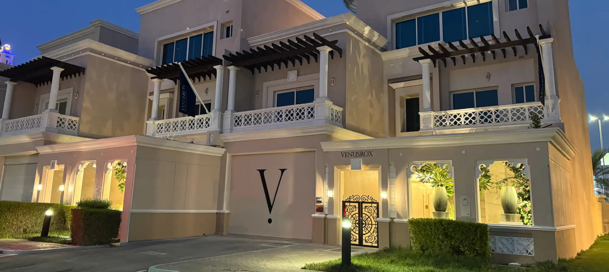 The building features a beige exterior with white decorative railings and columns, illuminated by warm lighting at dusk.