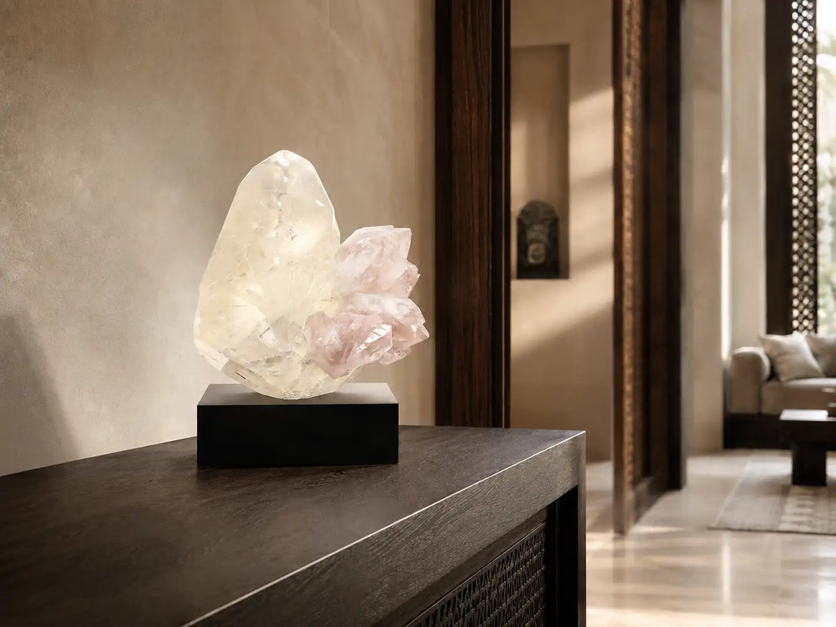 A translucent, crystalline geode lamp with a soft pink quartz cluster resting on a sleek black base.