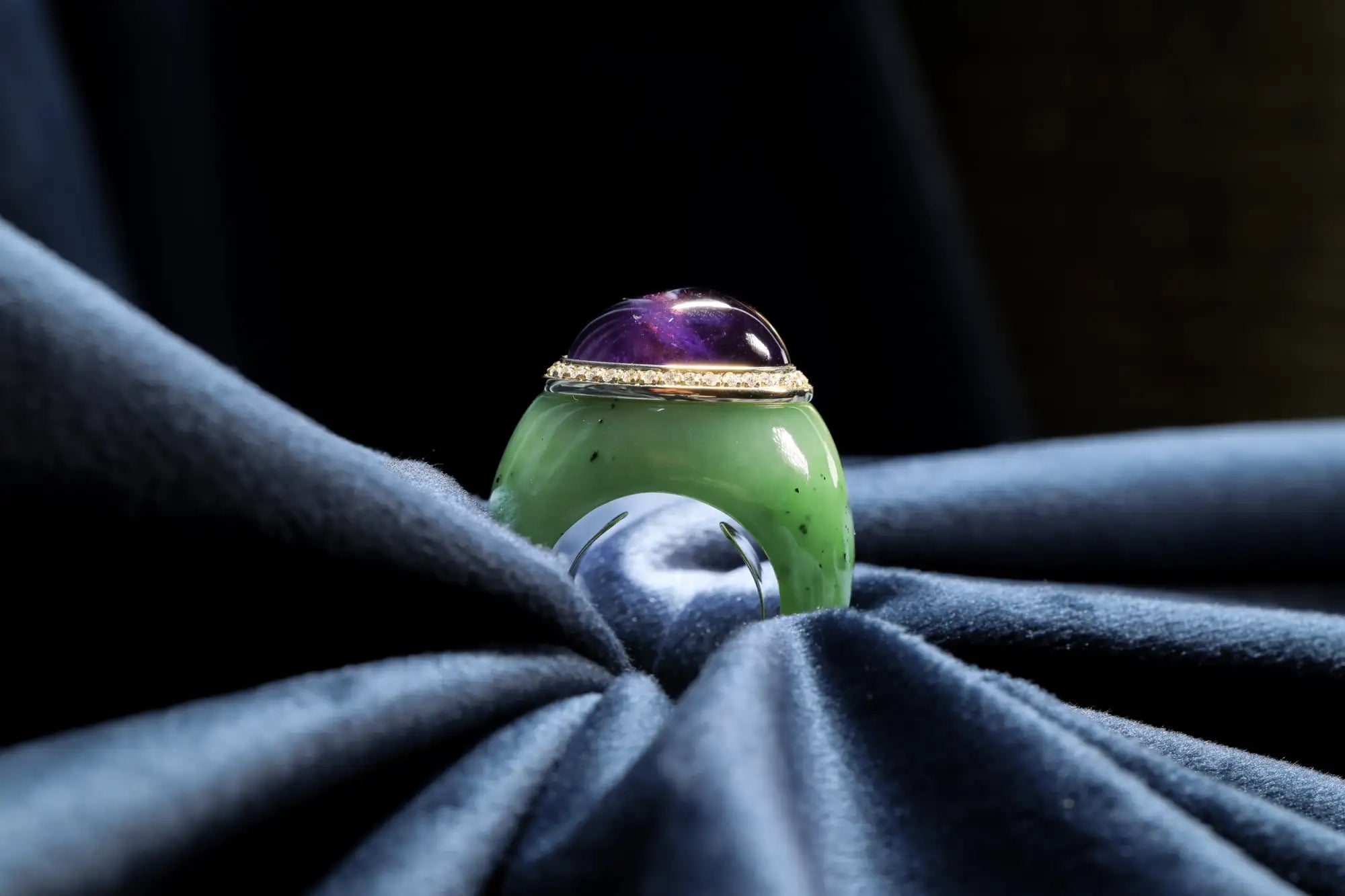 A vibrant green jade ring with a polished, dome-shaped amethyst cabochon set in a gold-toned bezel.